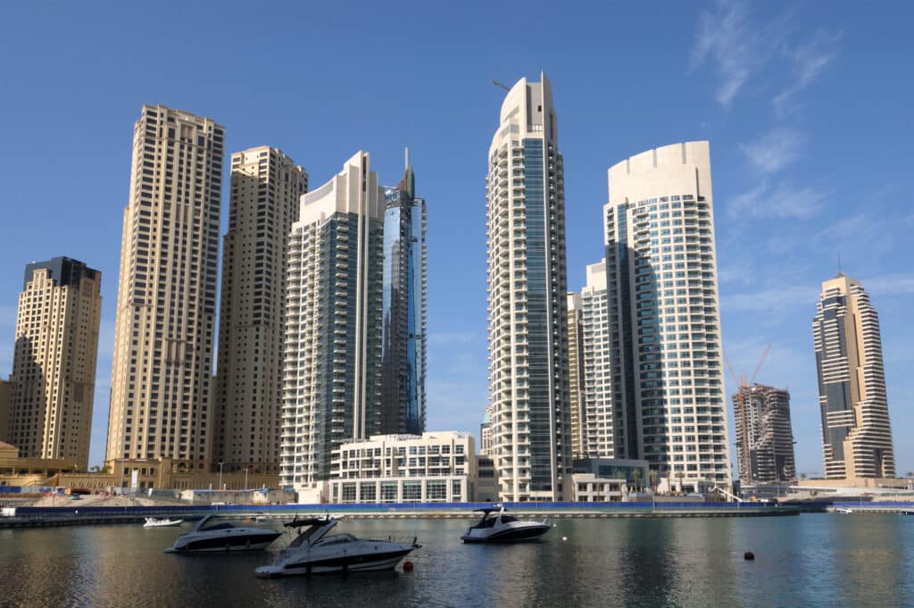 Gratte-ciel et Bateaux à Dubai Marina Vue de hauts immeubles modernes et de bateaux dans une marina ensoleillée.
